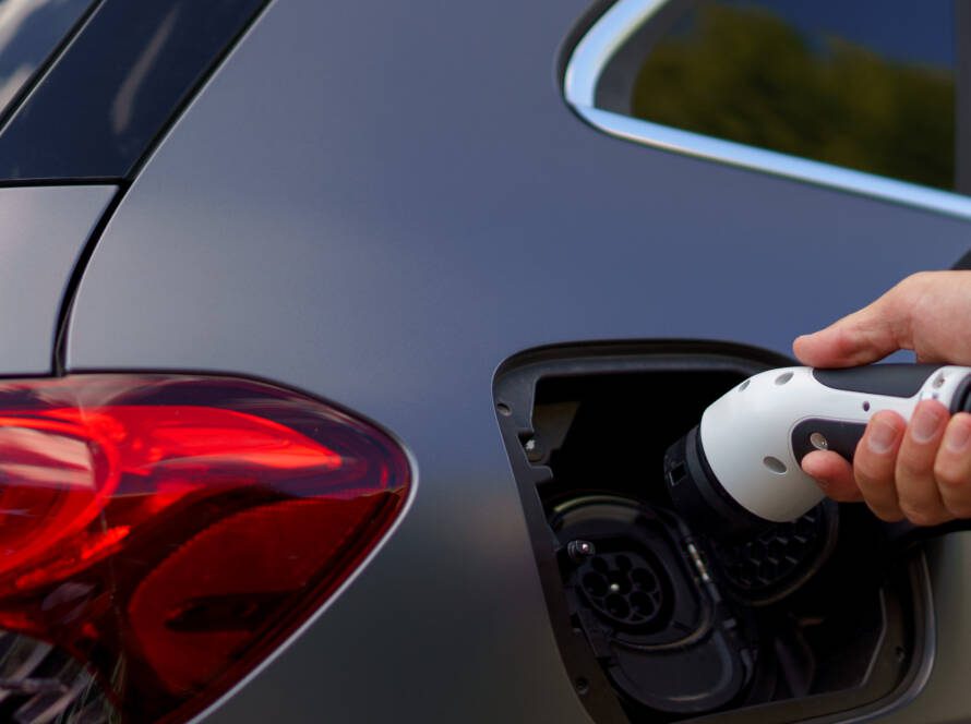 Man holding power supply cable at electric vehicle charging station, closeup