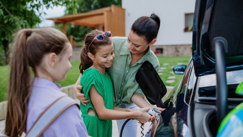 Happy mother showing her little daughters how to charge their electric car.