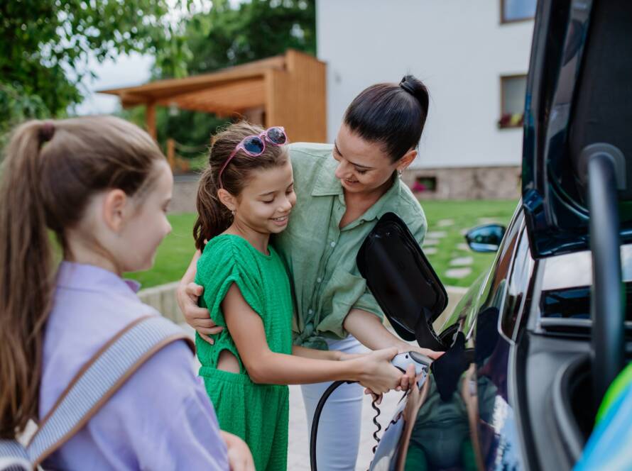 Happy mother showing her little daughters how to charge their electric car.